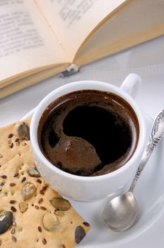 Cup of coffee and crackers on a table with an open book