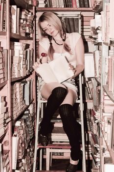teen girl reading a book in the library among the bookshelves   toning soft focus