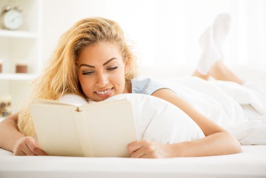 Cute young beautiful woman reading book in the bed