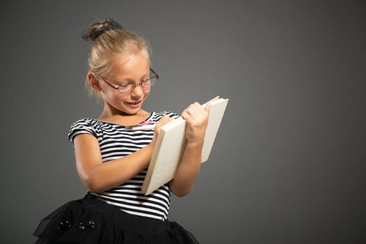 Pretty little girl smiling and posing with book. Studio shutting. Grey background. 