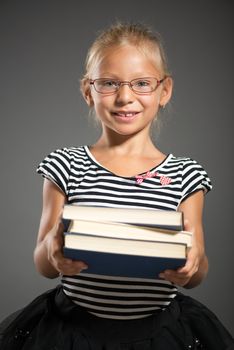 Cute little girl standing and holding books. Studio shutting. Grey background. Looking at camera.
