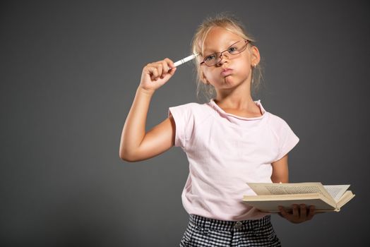 Thinking Cute little girl standing and holding book. Studio shutting. Grey background. Looking at camera.