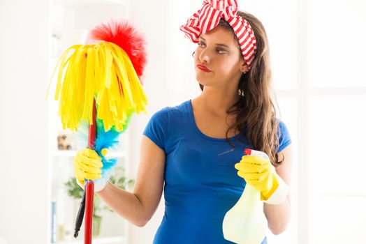Portrait of a young beautiful unhappy maid holding a cleaning equipment. 