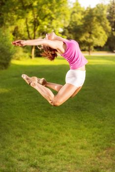 Cute sporty young woman jumping in the park.