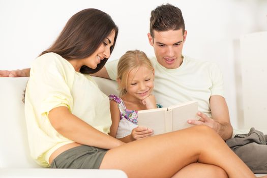 Beautiful Happy young mother and father and their cute daughter sitting at home and reading book