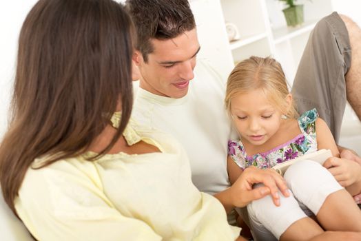 Beautiful Happy young mother and father and their cute daughter sitting at home and reading book