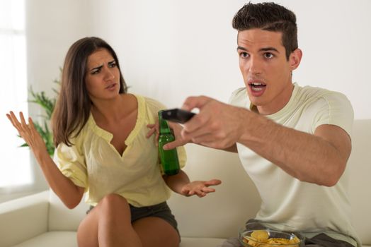 Young man sitting on sofa and watching tv. His angry wife yelling.