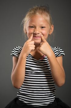 Pretty little girl smiling and posing. Studio shutting. Grey background. Looking at camera.