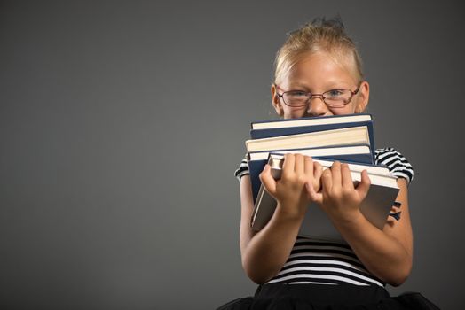 Cute little girl standing and holding books. Studio shutting. Grey background. Looking at camera.