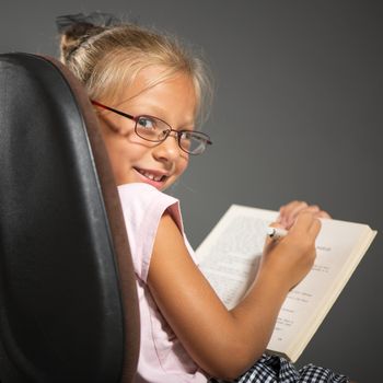 Cute little girl sitting and holding book. Studio shutting. Grey background. Looking at camera.