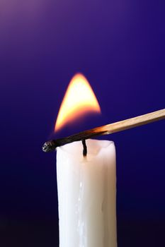 Closeup of candle inflamed with match on dark background