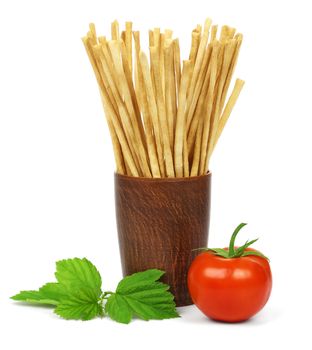 Crispy crunchy long bread sticks in a ceramic cup, a tomato and green leaves, isolated on a white background.