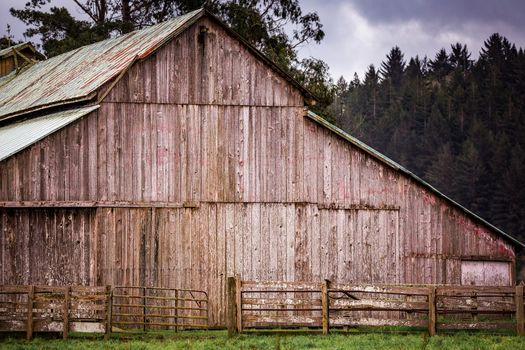 An old barn on a rural farm with trees, sky and clouds.