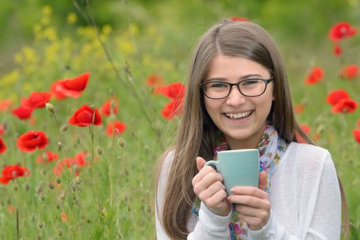 Teen girl drink cup of tea on poppy field
