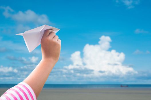 plane paper in children hand over seaand blue sky in cloudy day