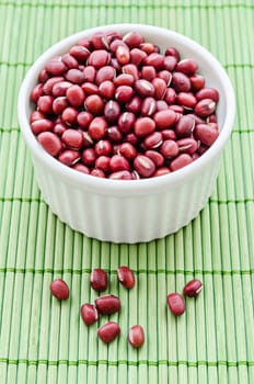 Raw azuki beans in white cup on green wooden mat.