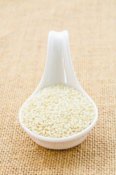 White sesame seeds in white spoon on sack background.