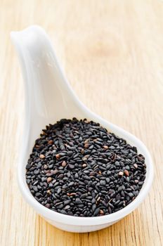 Black sesame seeds in white spoon on wood table.