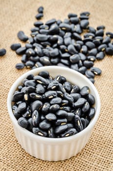 Black bean seeds in white cup on sack background.