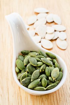 Peeled pumpkin seeds pour in white spoon on wood table.