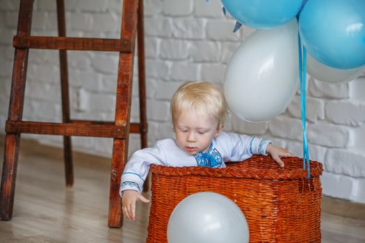 Little-year-old blond boy in traditional Ukrainian embroidered shirt playing with toys in the studio decorated