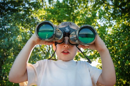 Little boy looking through binoculars on river bank