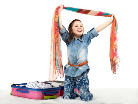 Fashionable little girl unpacking a suitcase isolated on white background