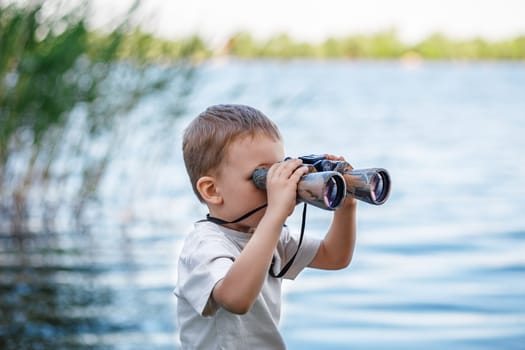 Little boy looking through binoculars on river bank