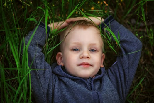 Portrait of a smiling blonde little boy lying on green grass