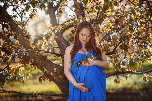 Portrait of Beautiful pregnant woman in the lush spring garden in full growth