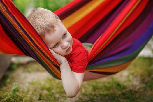 Beautiful cheerful little boy resting in a hammock striped textile