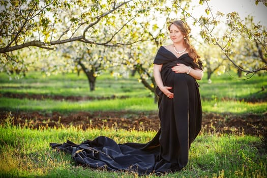 Beautiful pregnant woman in black in the lush spring garden in full growth