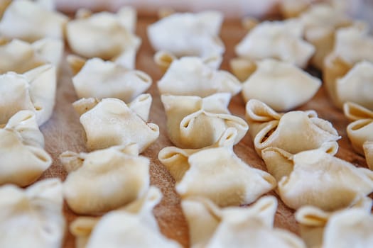 raw ravioli homemade manual molding lie on a wooden board. Ukrainian traditional dish pelmeni with raw meat. Cooking homemade dumplings.