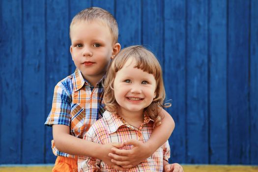 Portrait of happy joyful beautiful little boy and girl against the old textured blue wall