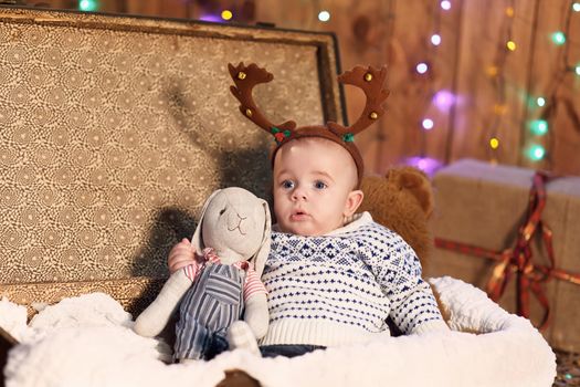 Little baby boy sitting in a suitcase with a toy bunny in the room with Christmas decorations