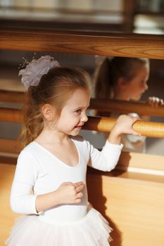 Ballerina little girl standing near mirror in the gym