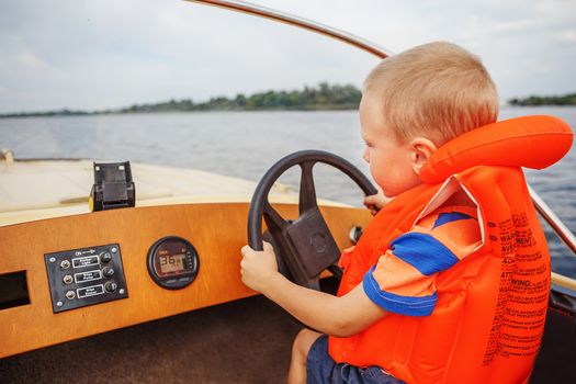 Little boy driving a motor boat on river firmly holding the steering wheel