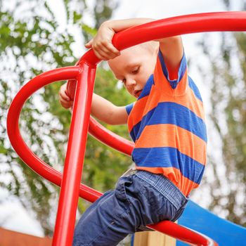 Cute little boy playing on the playground in the summer in the city