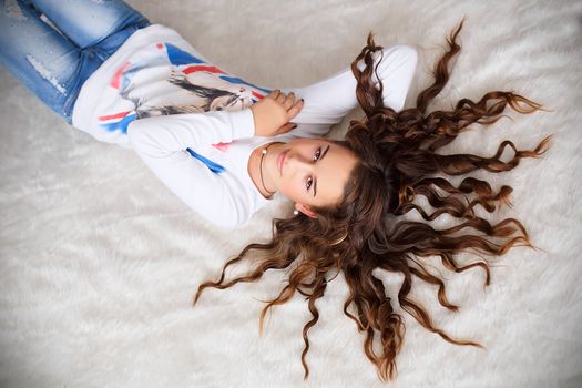 Portrait of a pretty teen girl lying on the floor with her long hair wavy
