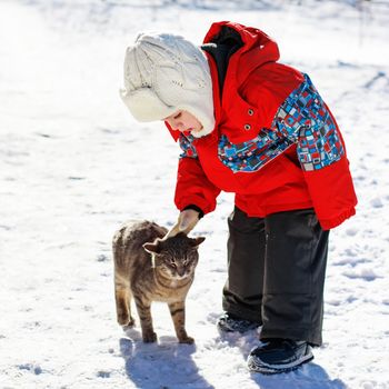 Little boy playing with the cat in the snow