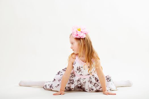 Little blond girl in a dress sitting on the twine against a white background. facial profile