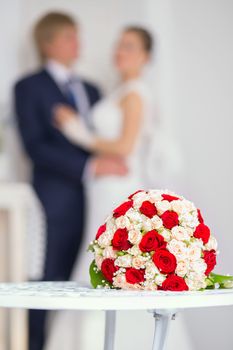Wedding bridal bouquet with red and white roses on the table against the background of the bride and groom. Wedding concept