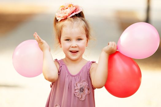 Portrait of laughing and playing little girl holding colorful balloons. Positive emitions. Happy child.