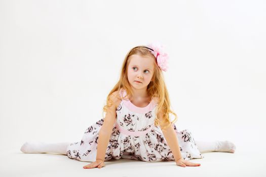 Little blond girl in a dress sitting on the twine in front of white background