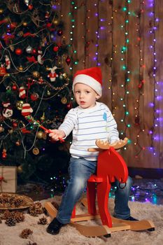 Little boy in a cap of Santa Claus riding a reindeer toy. The concept of Christmas and New Year