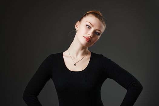 Portrait of a young beautiful girl in black on a gray background in the studio. Woman dancer or ballerina.