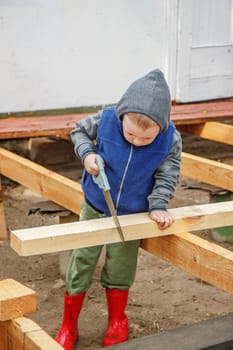 Little studious boy sawing a wooden board. Home construction. Little Helper. Little builder.