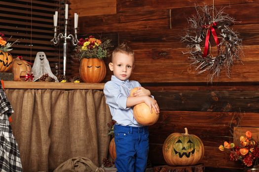 Cute Little Boy having fun in Halloween decorations. Halloween party with child holding painted pumpkin