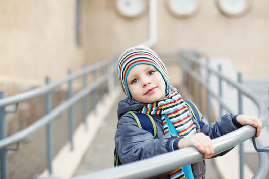 Beautiful little boy in bright striped hat and scarf outdoors near the school building