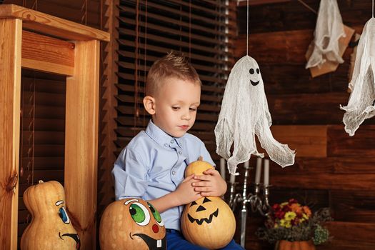 Cute Little Boy having fun in Halloween decorations. Halloween party with child holding painted pumpkin